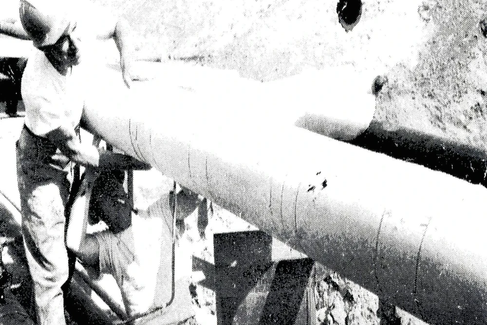 Workers insulate an outdoor pipe before installing sheet metal lagging. Neither tradesman is wearing a protective mask, and there are no warnings on the boxes indicating that this work is dangerous.