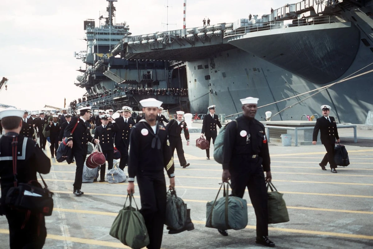 Navy personnel carrying their bags walk along the pier after disembarking the aircraft carrier